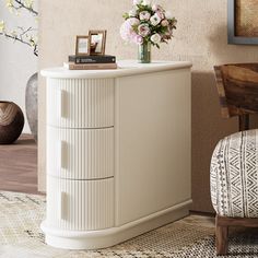 a white cabinet with flowers on top in a room next to a chair and table