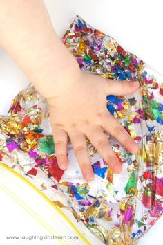 a child's hand reaching into a pile of confetti paper with the words sensory glitter blob on it