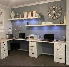 a desk with two computers on it and a large clock mounted to the wall behind it