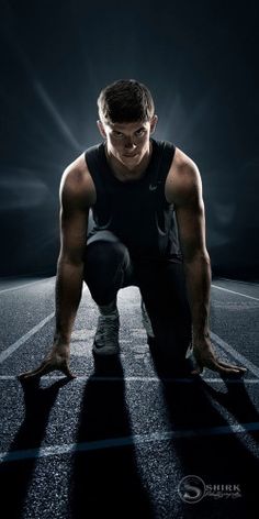 a man squatting down in the middle of a race track with his shadow on the ground