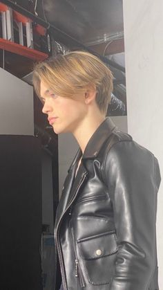 a woman in a black leather jacket is looking at something on the shelf behind her