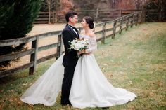 a bride and groom standing next to each other in front of a fence with trees