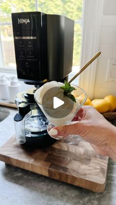 a person holding up a drink in front of an espresso machine and blender