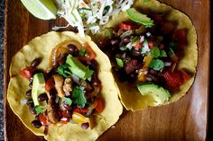 two tacos with beans, avocado and shredded cheese on a wooden tray