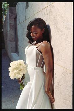 a woman in a wedding dress leaning against a wall holding a bouquet of white flowers