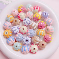 a white bowl filled with lots of colorful beads on top of a pink tablecloth