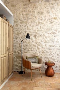 a living room with a chair, lamp and cupboards in front of a stone wall