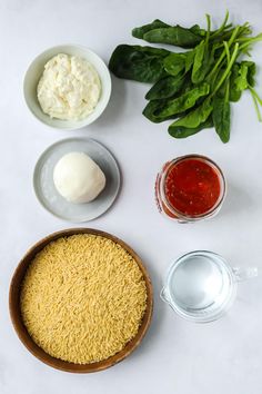 ingredients to make an appetizer laid out on a white surface including spinach, cheese and sauces