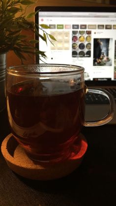 a cup of tea sitting on top of a wooden coaster next to a laptop computer