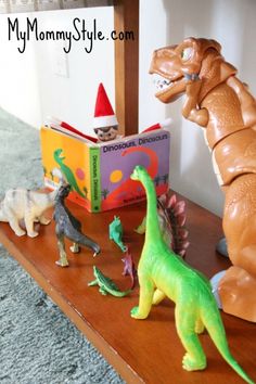 several toy dinosaurs on a shelf in front of a book