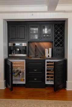 an empty kitchen with black cabinets and wine bottles in the fridge door open to show what's inside