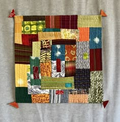 a patchwork quilt with orange and green accents on a gray background, hanging from an orange hook