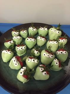 some green apples with googly eyes and strawberries on them sitting on a black plate