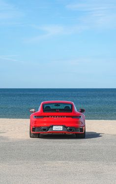 a red sports car parked on the beach next to the ocean in front of a blue sky