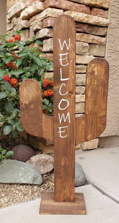 a wooden welcome sign sitting on top of a sidewalk next to a planter filled with flowers