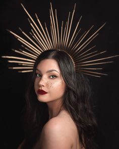 a woman with long hair wearing a gold headpiece and red lipstick in front of a black background