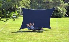 a man laying on top of a lawn chair under a blue tarp in the middle of a field