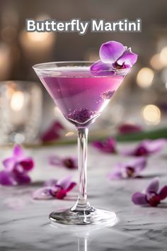 a purple drink in a martini glass with pink flowers on the table behind it and text that reads, butterfly martini