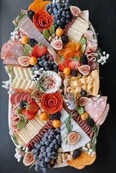 an assortment of cheeses, fruits and meats arranged in a circle on a black surface