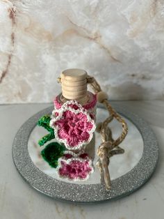 a crocheted bottle on a plate with a wooden spool and flower decoration