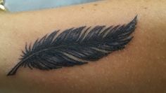 a black feather tattoo on the arm