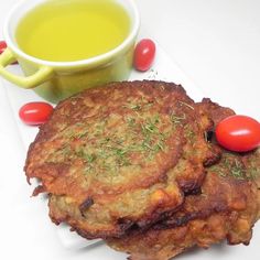 two crab cakes on a plate next to a cup of green tea and cherry tomatoes