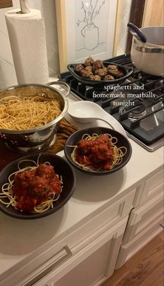 three plates of spaghetti and meatballs on a kitchen counter