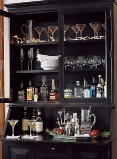 a black cabinet filled with lots of bottles and glasses on top of it's shelves