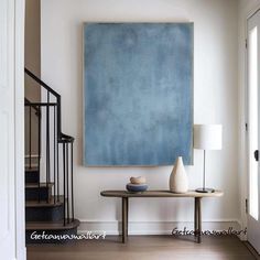 a blue painting hangs on the wall above a table with two vases and a lamp