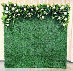 an artificial grass wall with white flowers on top and greenery growing up the side