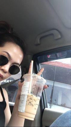 a woman in sunglasses is holding up a drink and looking at the camera while sitting in a car