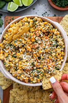 a hand holding a tortilla chip and dipping it into a bowl filled with corn salsa