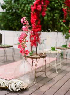 pink flowers in vases and chairs on the ground near red bougaia plants