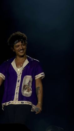 a male in a purple shirt and black pants on stage with his hands out to the side