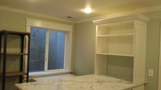 an empty room with marble counter tops and shelves in the corner, next to a window