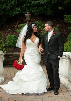 a bride and groom standing on a bridge in front of some bushes with red flowers