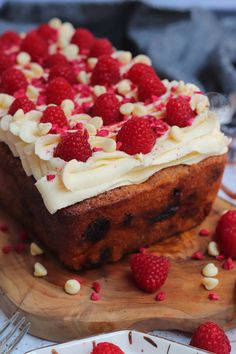 a piece of cake with white frosting and raspberries on a cutting board