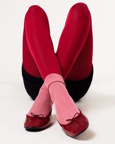 the legs and feet of a woman wearing red stockings with bows on them, sitting in front of a white background