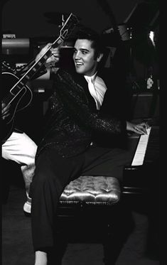 elvis presley is sitting on a piano and playing the guitar in front of an instrument