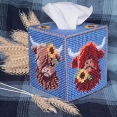 a cross stitch tissue box sitting on top of a blue plaid blanket with two cows