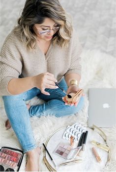 a woman sitting on the floor with makeup and eyeliners in front of her