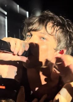 a young man holding a cell phone up to his face while standing in front of a crowd