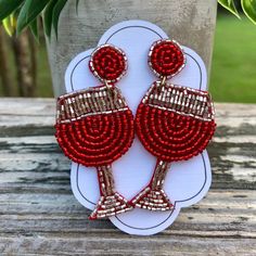 two red beaded earrings sitting on top of a wooden table next to a potted plant