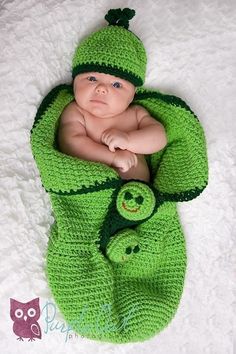 a baby in a green crochet outfit laying on top of a white blanket