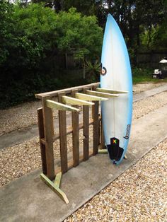 a blue surfboard sitting on top of a wooden stand next to a gravel road