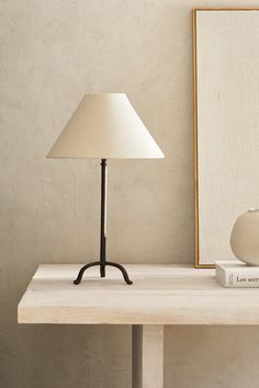 a lamp sitting on top of a wooden table next to a white vase and book