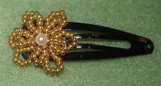 a black comb with gold beads and a pearl brooch sitting on a green surface