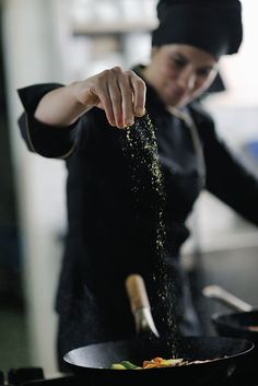 a woman is sprinkling some food in a frying pan