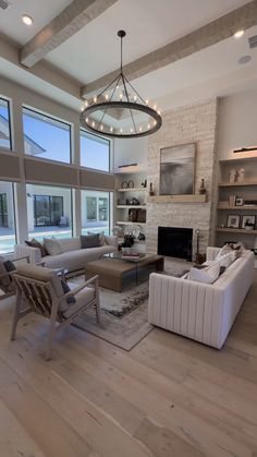 a living room filled with furniture and a fire place under a chandelier in front of large windows