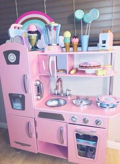 a pink play kitchen with ice cream and cupcakes on the top shelf next to it